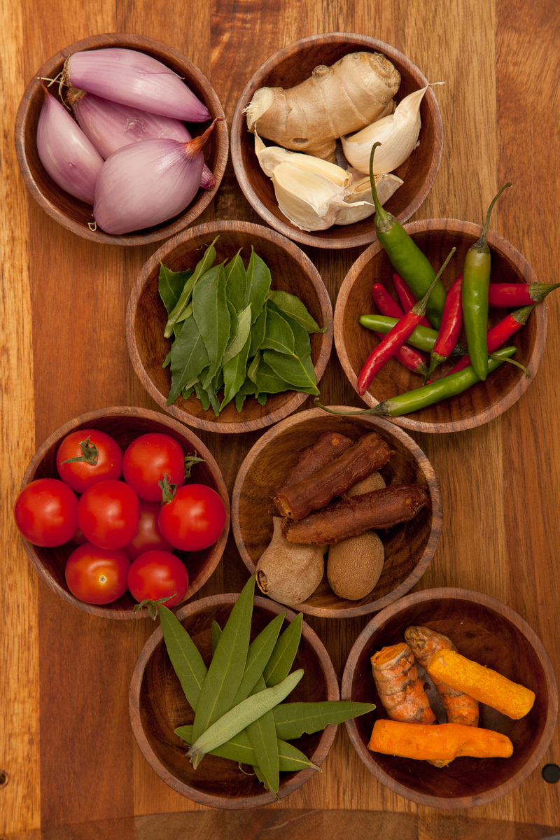 Fresh ingredients common in curries from left to right: (top) shallots, ginger, garlic; (second row) curry leaves, red and green Thai chilies; (third row) tomatoes, peeled and unpeeled fresh tamarind; (bottom) fresh bay leaves, and turmeric root.