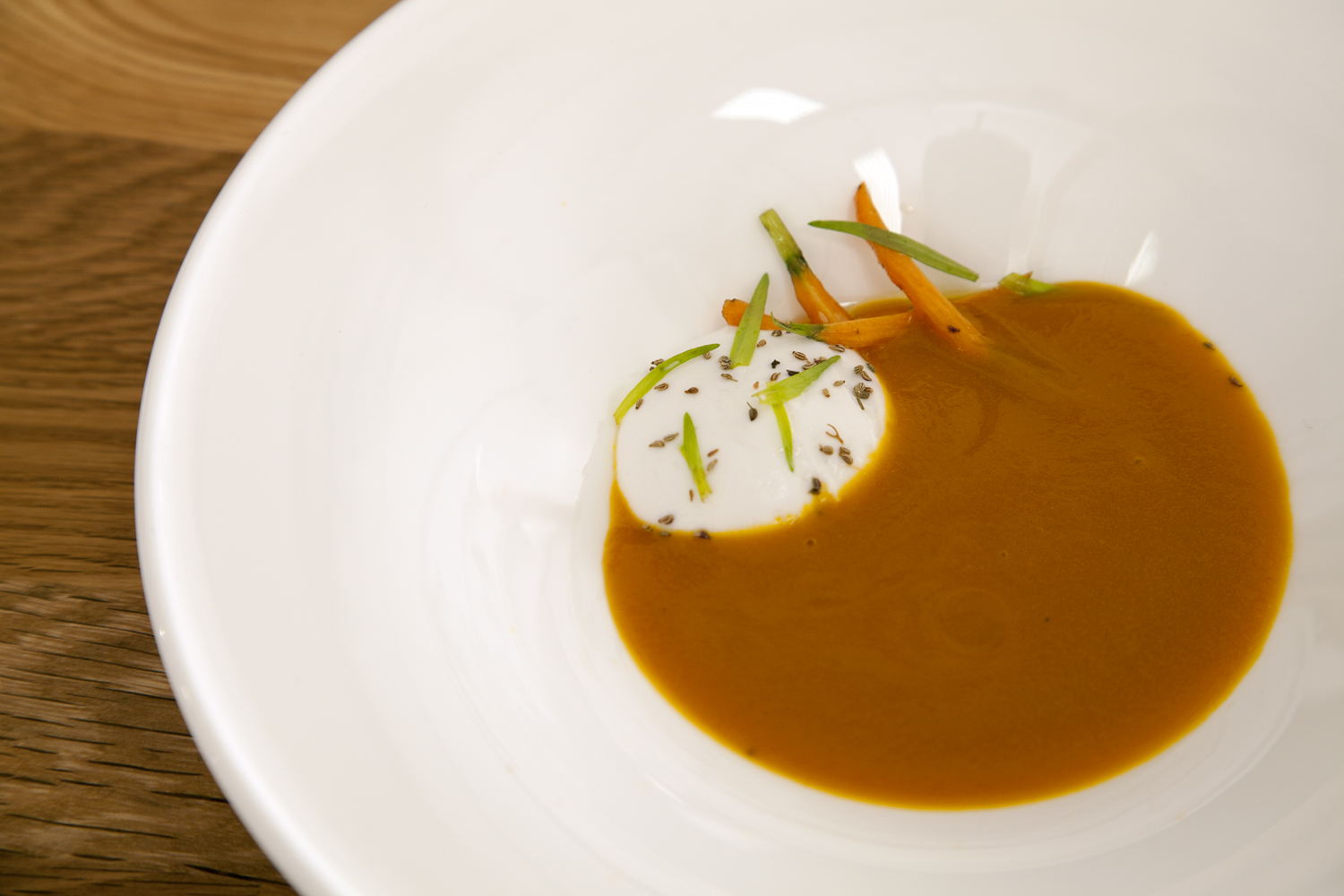 Caramelized carrot soup plated with coconut chutney foam, ajowan seeds, fresh tarragon, and baby carrots.
